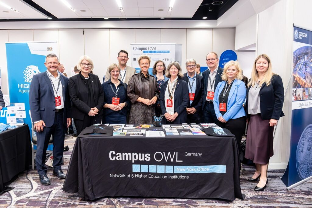 Foto von Männern und Frauen, die auf einer Tagung um einen Tisch von Campus OWL stehen.