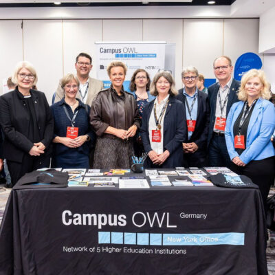 Foto von Männern und Frauen, die auf einer Tagung um einen Tisch von Campus OWL stehen.