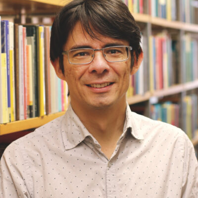 Mann mit braunen Haaren und Brille vor einem Bücherregal.