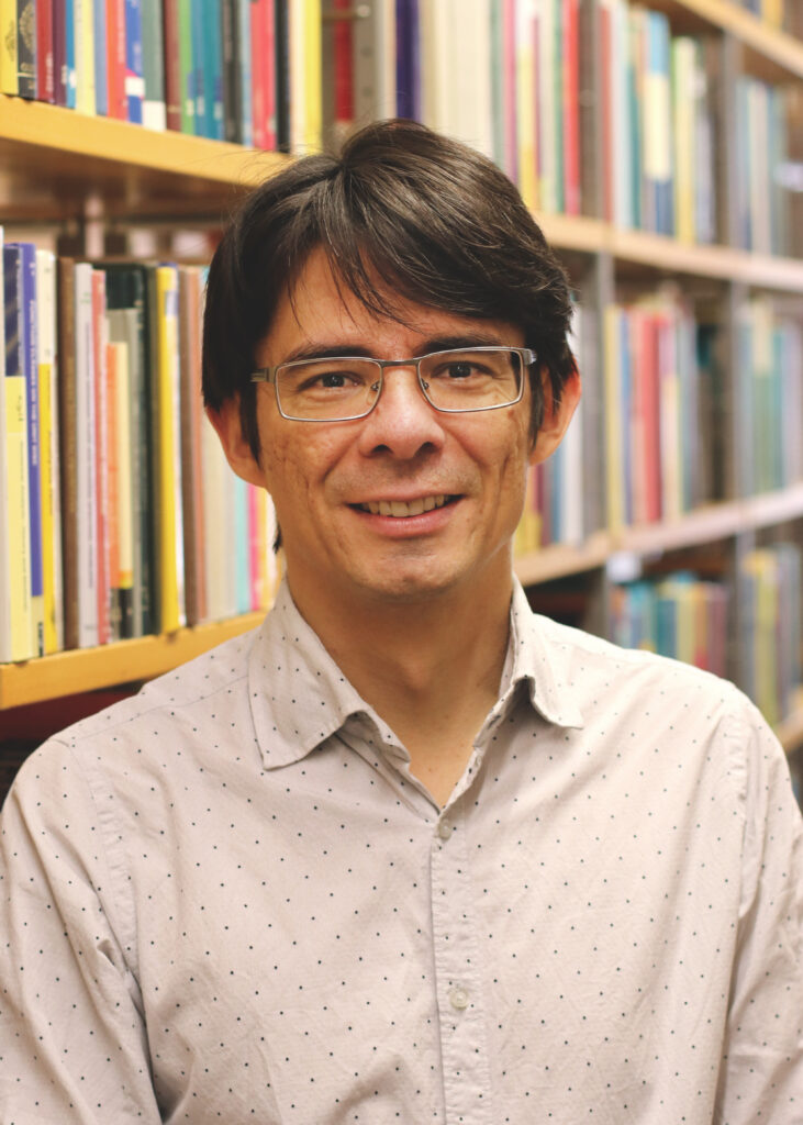 Mann mit braunen Haaren und Brille vor einem Bücherregal.