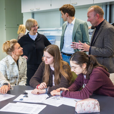NRW-Wissenschaftsministerin Ina Brandes (2. v. l.) schaut sich in den teutolabs gemeinsam mit Rektorin Professorin Dr. Angelika Epple (3. v. l.) die Arbeit von den Professor Dr. Claas Wegner (r.) an. Schüler*innen arbeiten in diesem Workshop zum Thema Stress.